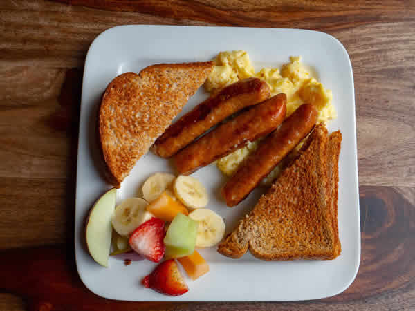 image: overhead view of plate with toast, sausages, eggs and fruit